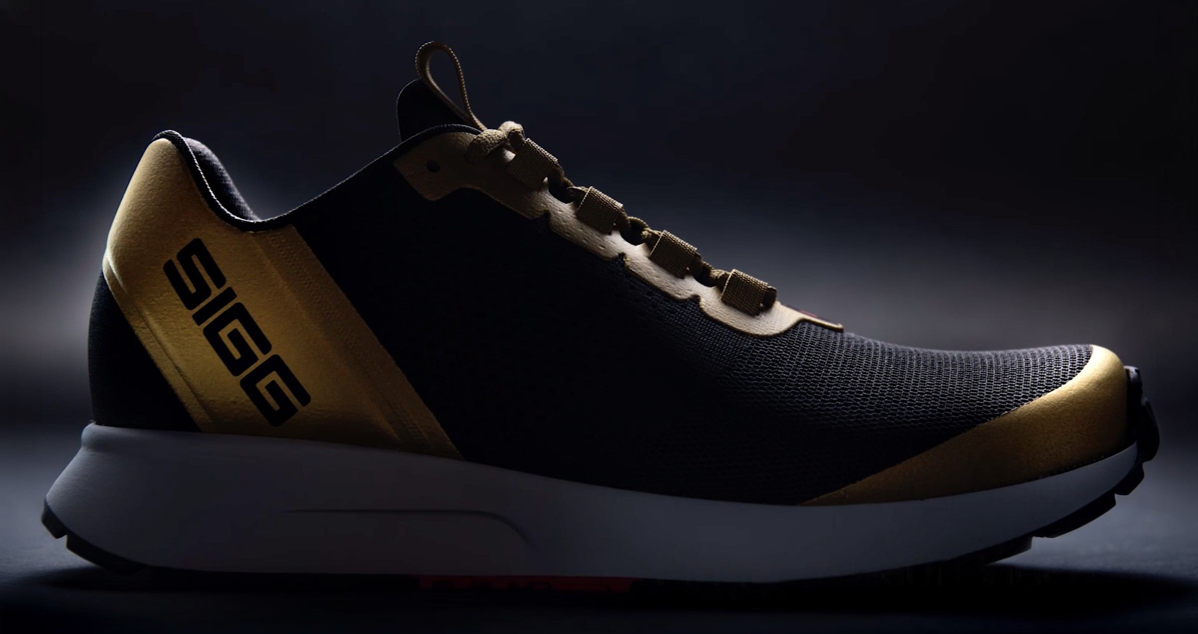 3D rendering of the shoe in black knit with a gold heel band, SIGG wordmark, and gold toe cap, lateral view on a dark backdrop.