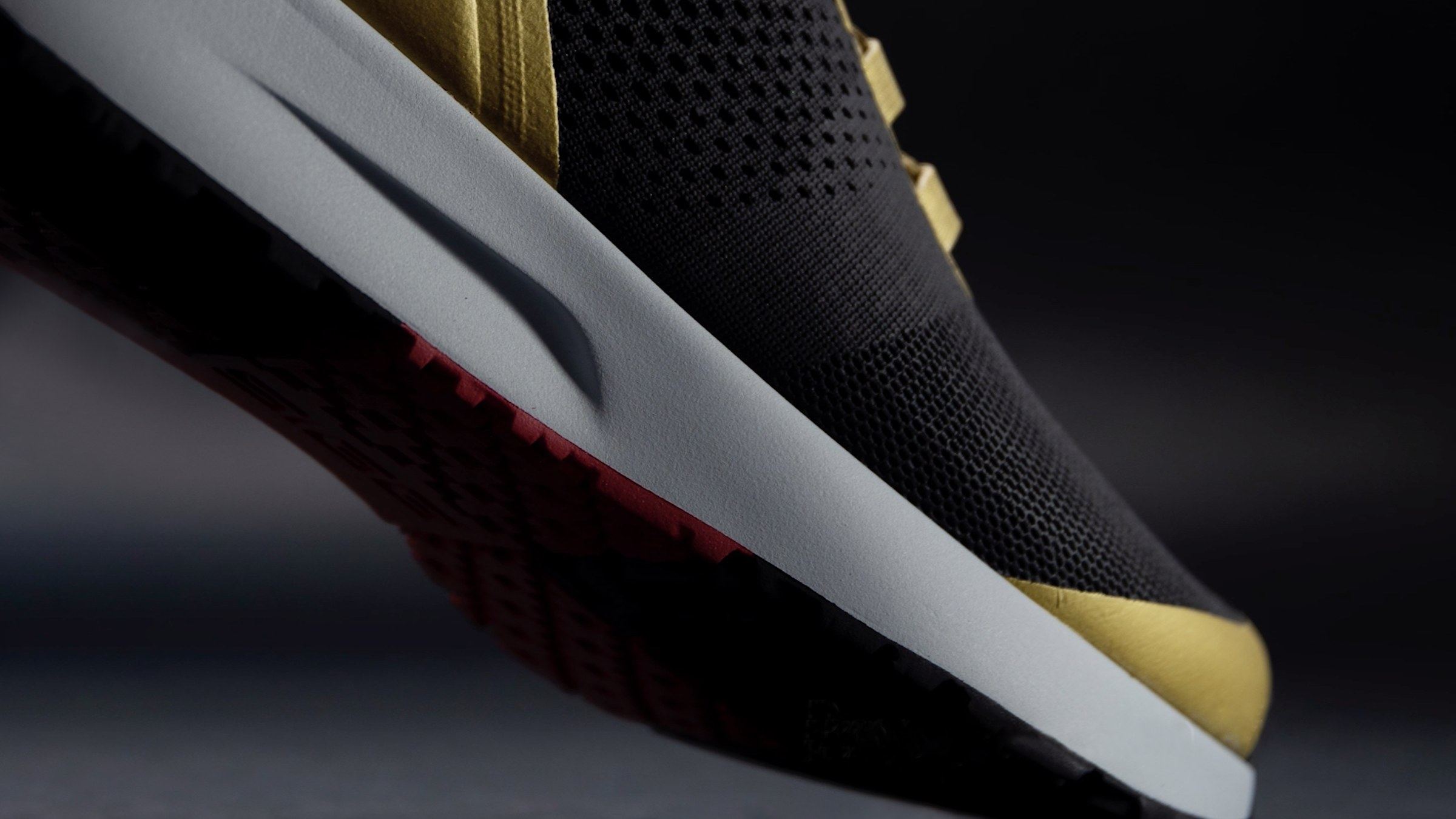 Close-up of the black and gold shoe's white midsole and red outsole from below.