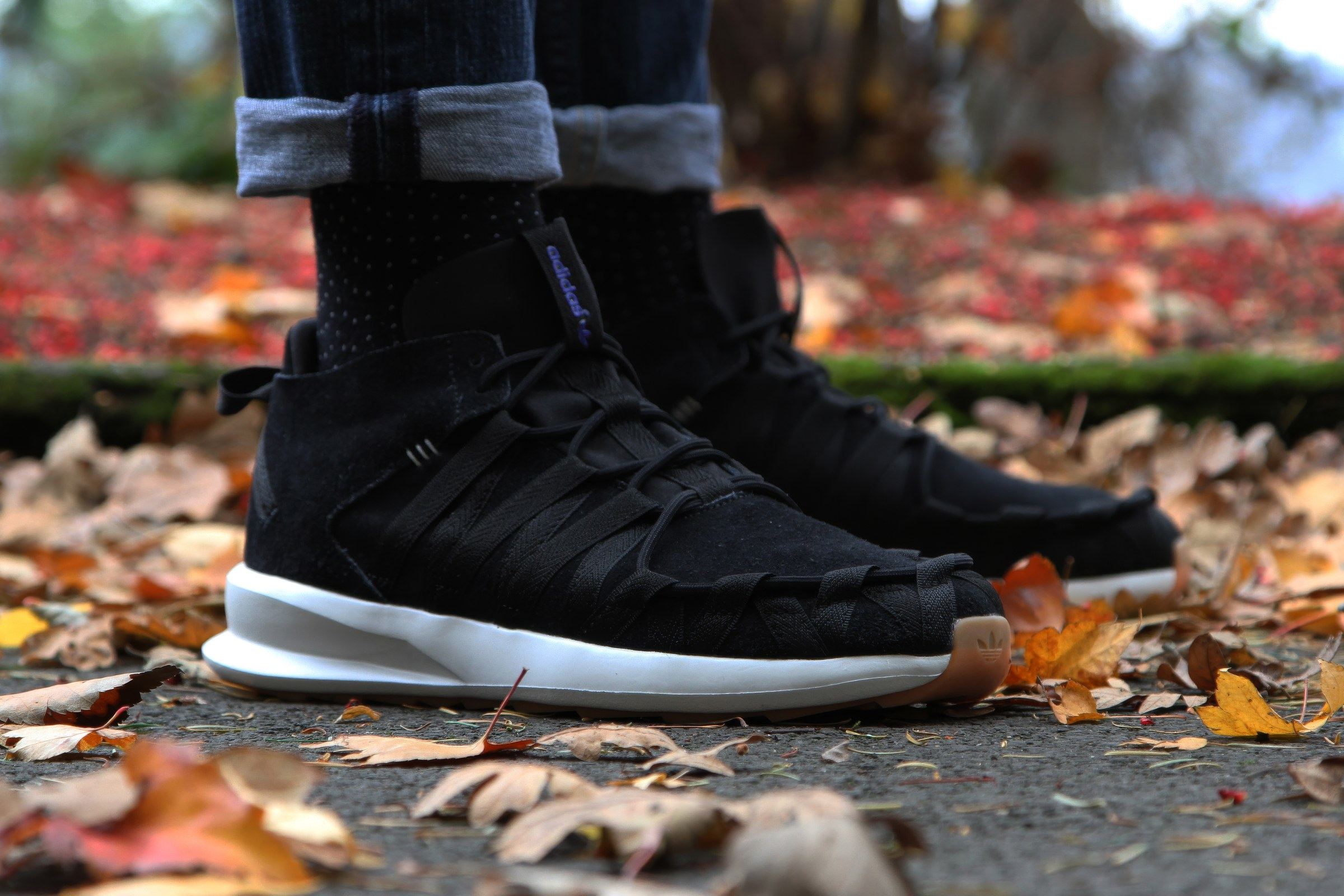 The black SL Loop Moc on foot with dark socks and rolled jeans, on fallen leaves.