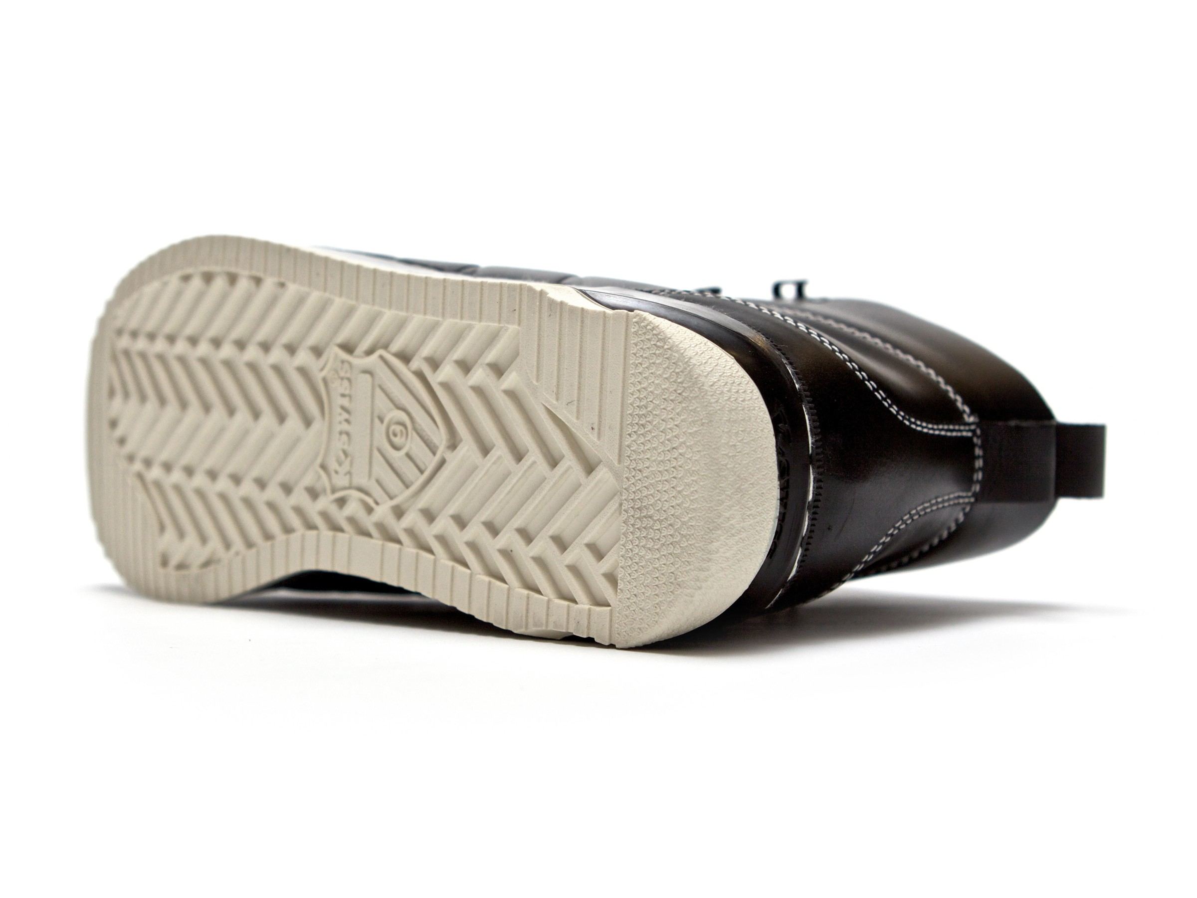 The black boot turned over to show the tan lug outsole with a K-Swiss shield.