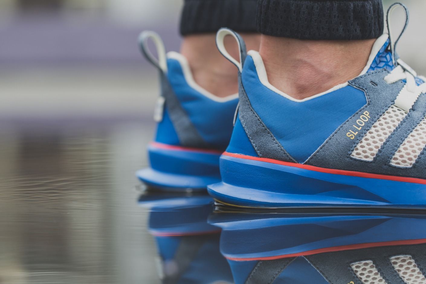 Heels of the blue suede pair with SL Loop printed on the heel, reflected in water.