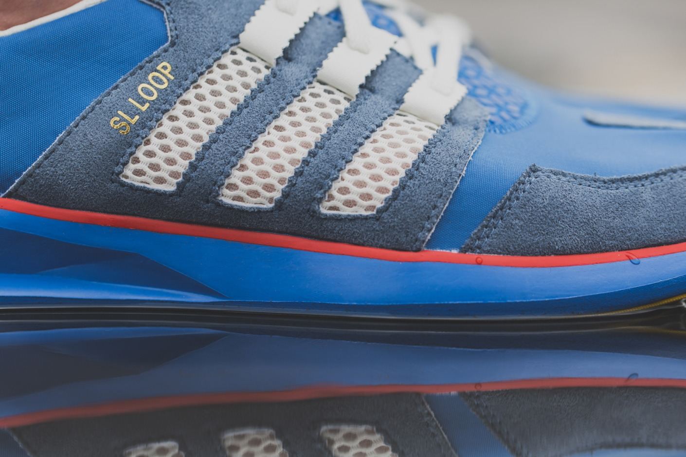 SL Loop Runner in blue suede and white mesh stripes with a red midsole line, lateral view reflected in water.