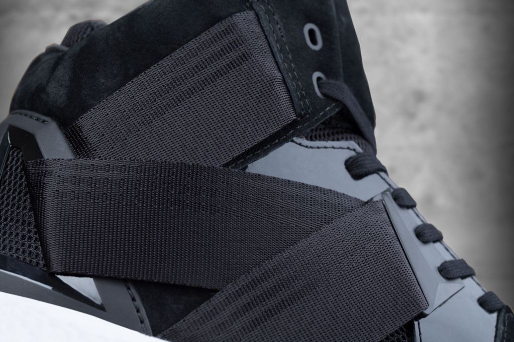 Close-up of the black webbing strap over the suede and mesh upper.