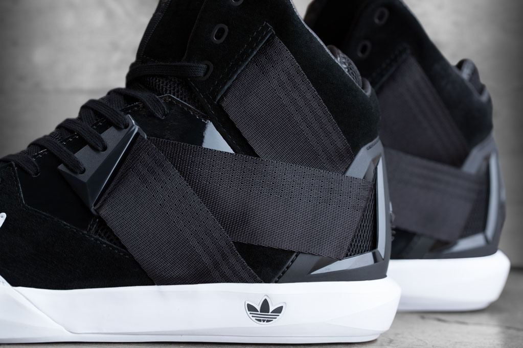 The black pair from the side, with the strap crossing the suede upper above the white midsole.