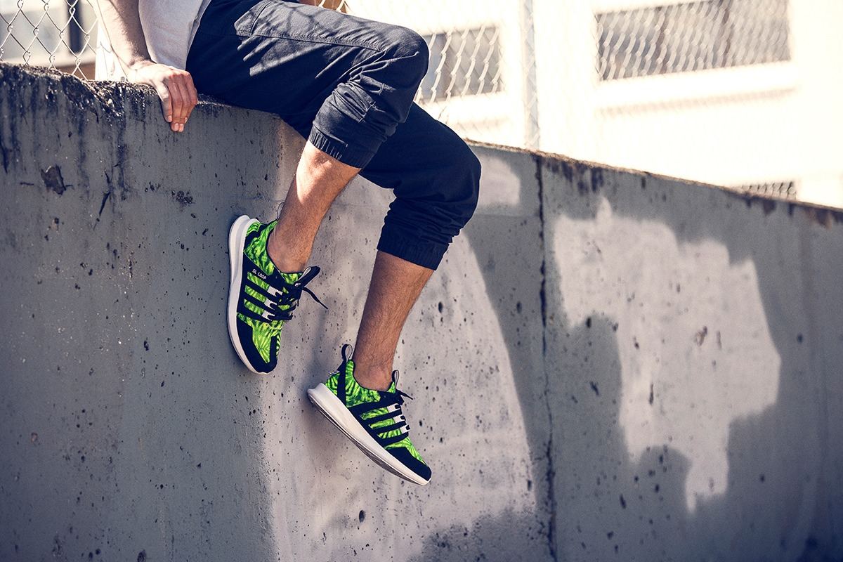 Someone sitting on a concrete wall wearing the green palm print SL Loop Runner.