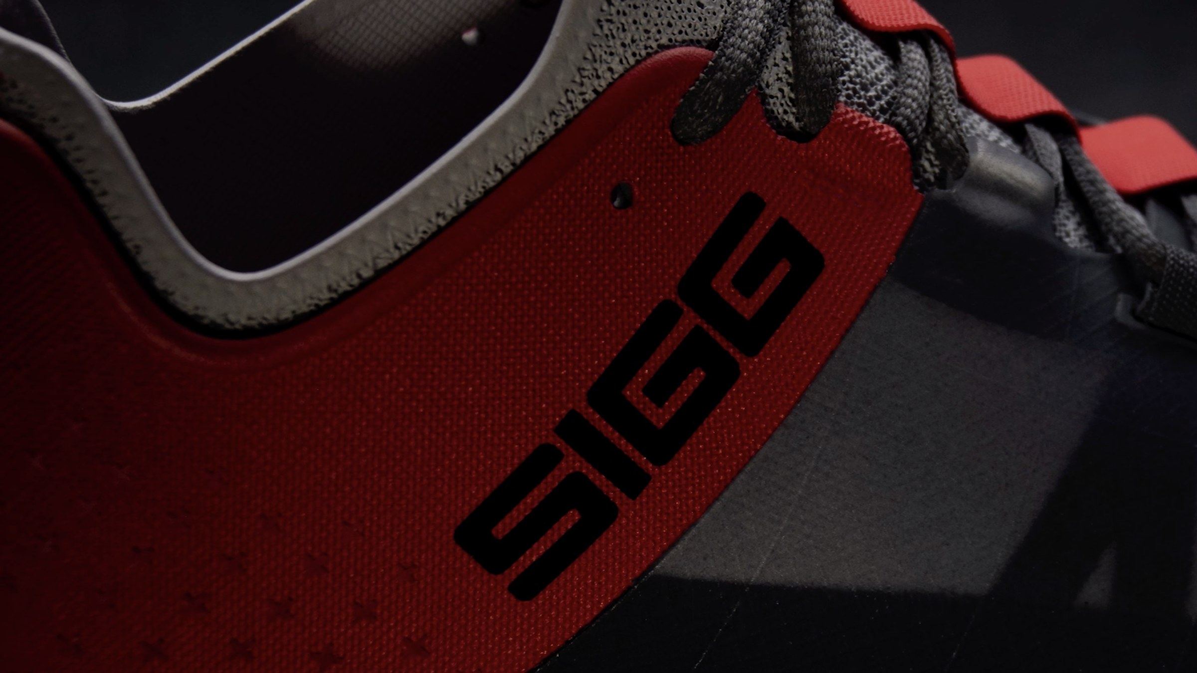 Close-up of the grey and red shoe's red heel with a black SIGG wordmark and grey laces.