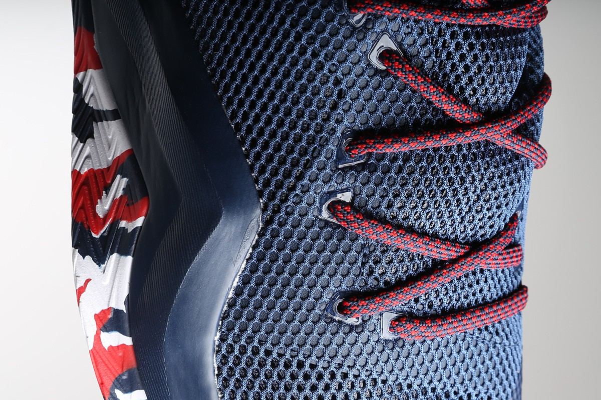 Close-up of the red laces crossing the navy mesh upper beside the camo outsole.