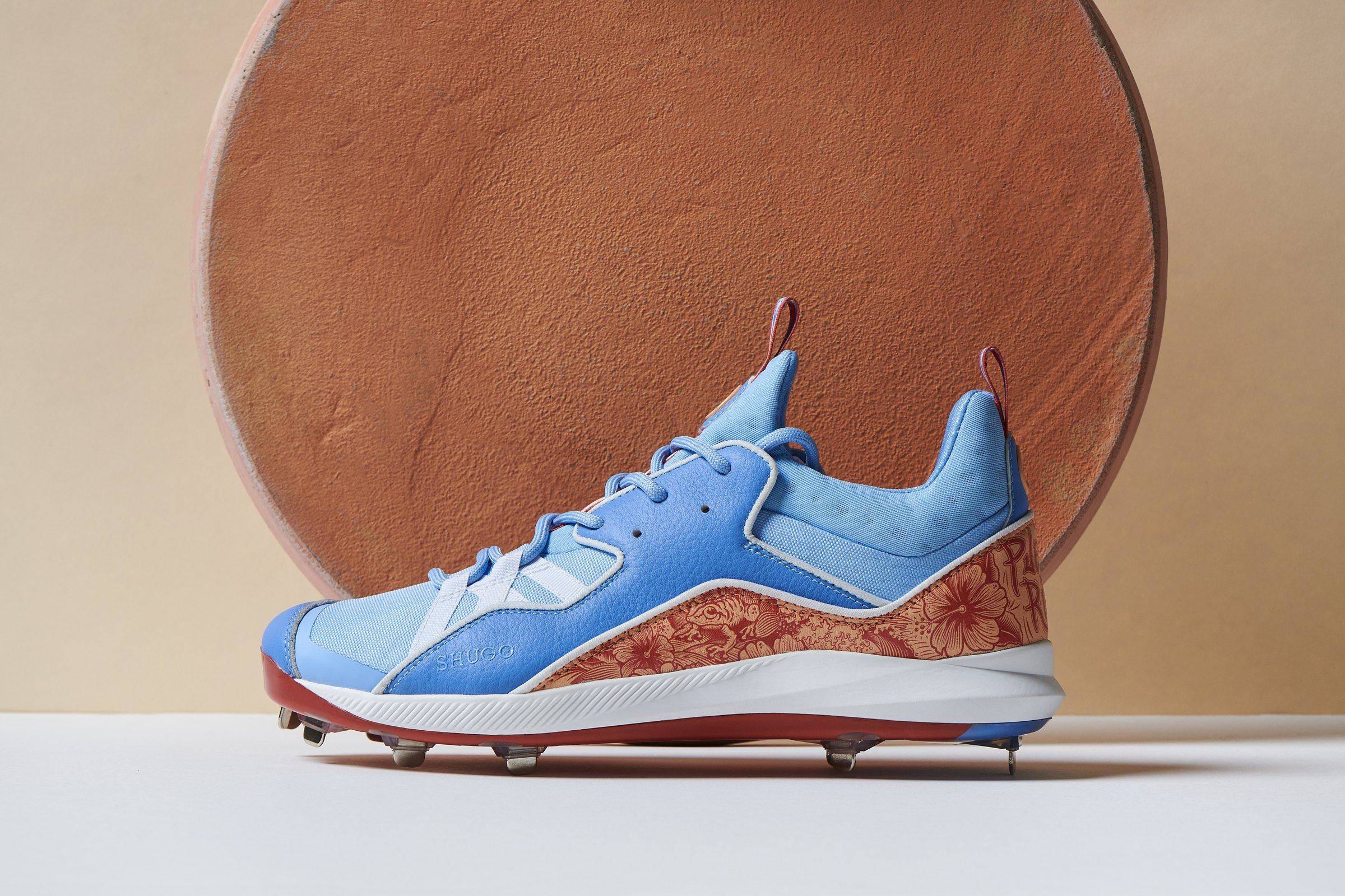 The Puerto Rico Zero in sky blue with a coral hibiscus print on the heel and a red plate, lateral view in front of a terracotta disc.
