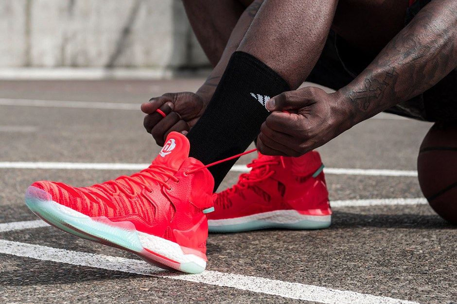A player lacing up the red D Rose 7 on an outdoor court.