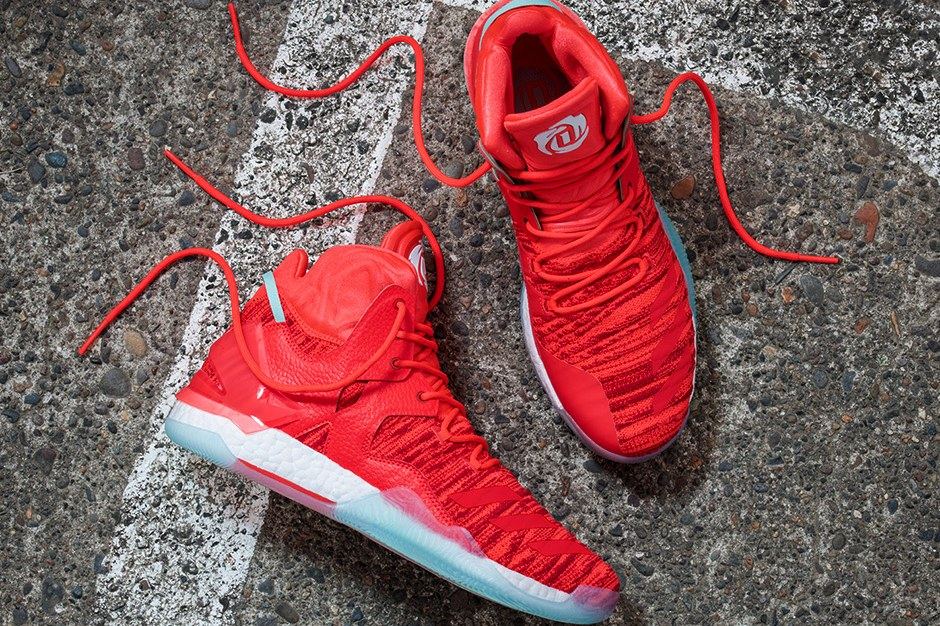 A pair of red D Rose 7s on asphalt, one on its side and one from above, with red laces and an icy blue translucent outsole.