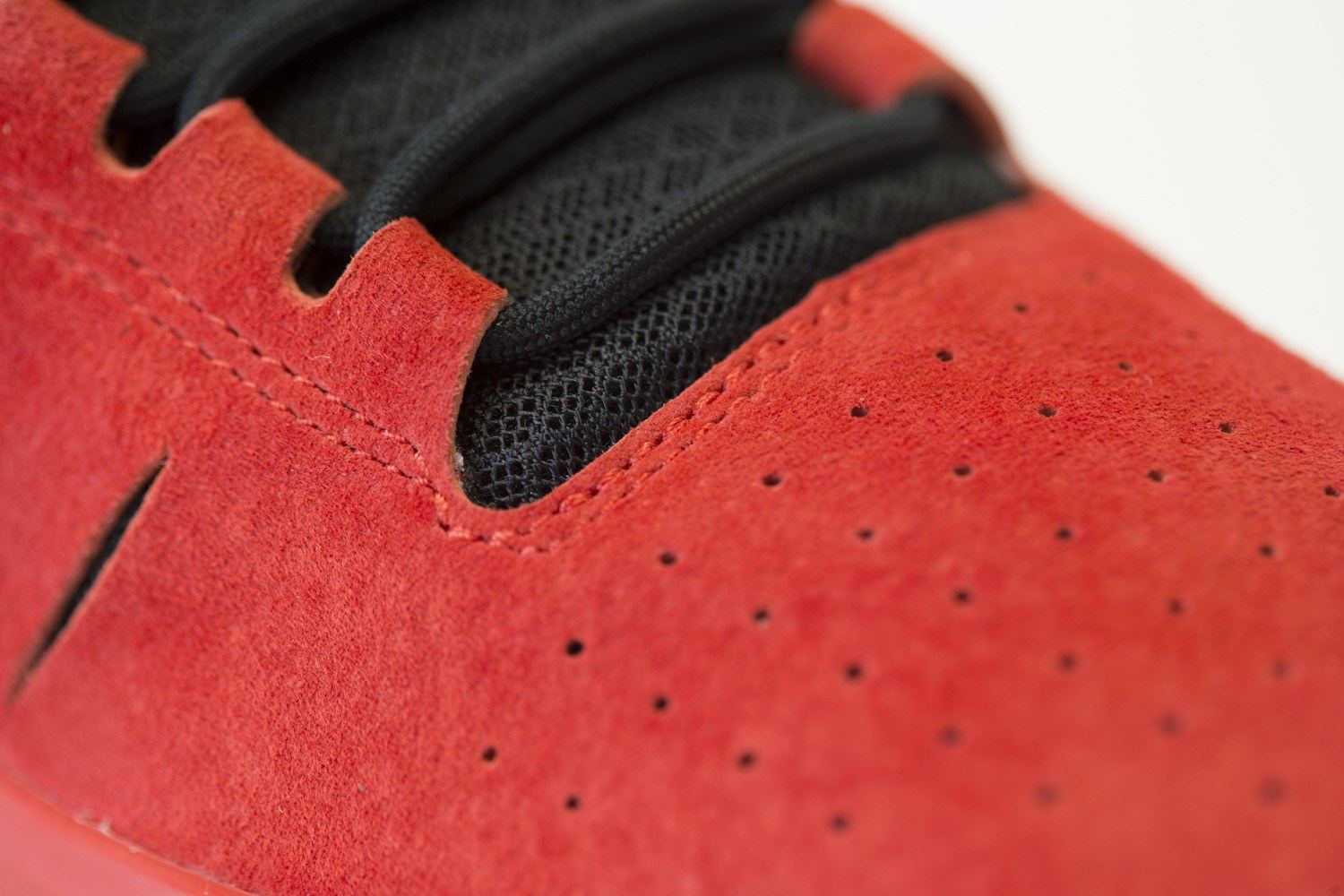 Close-up of the perforated red suede, slotted stripes and black mesh at the collar.