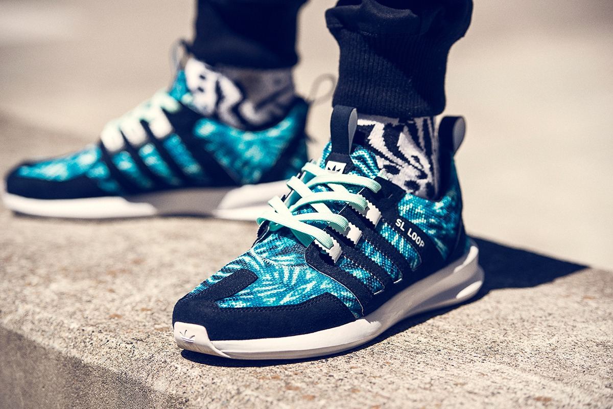 The teal palm print SL Loop Runner worn with white laces on a concrete ledge.