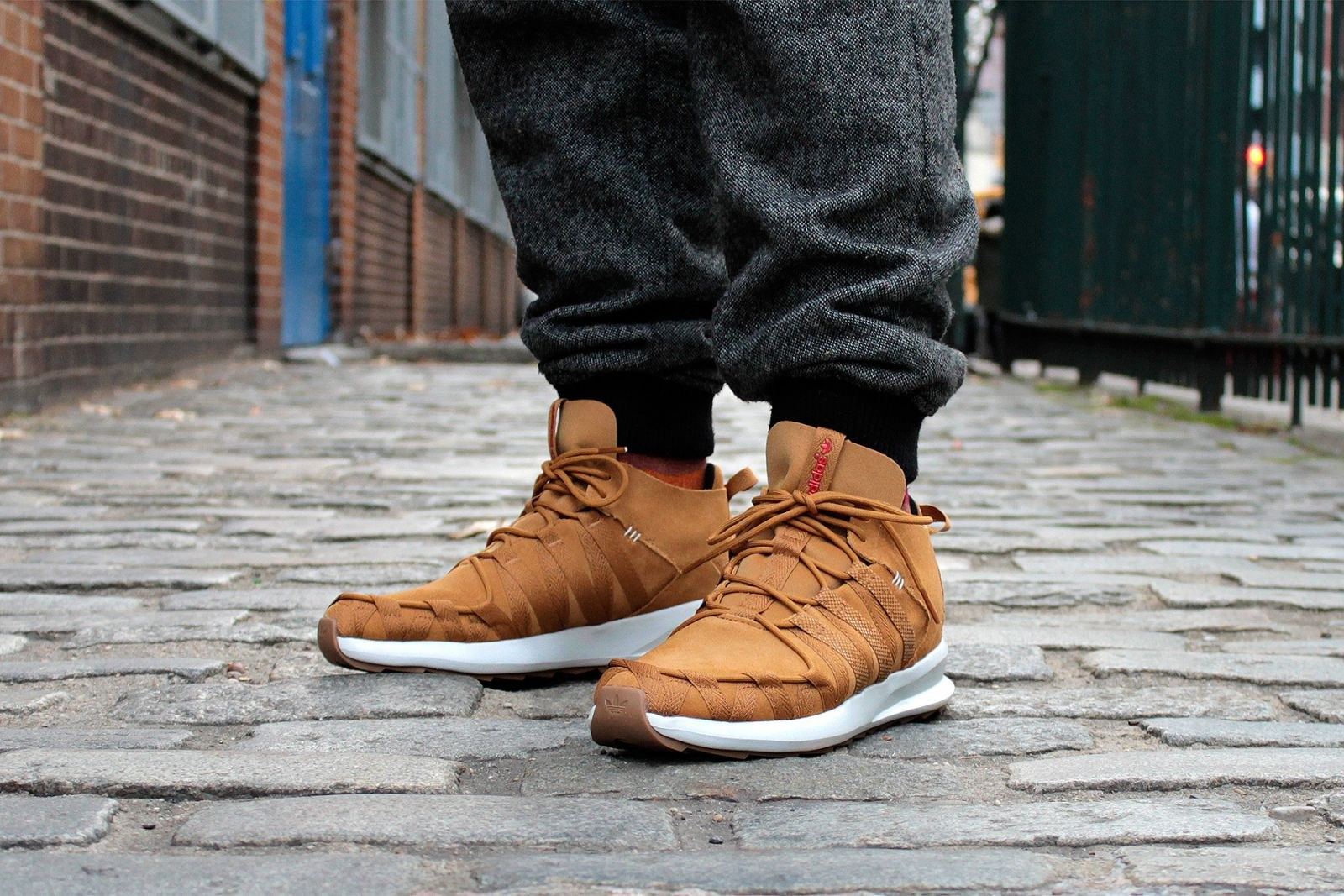 The wheat colorway on foot with grey joggers, on a brick sidewalk.