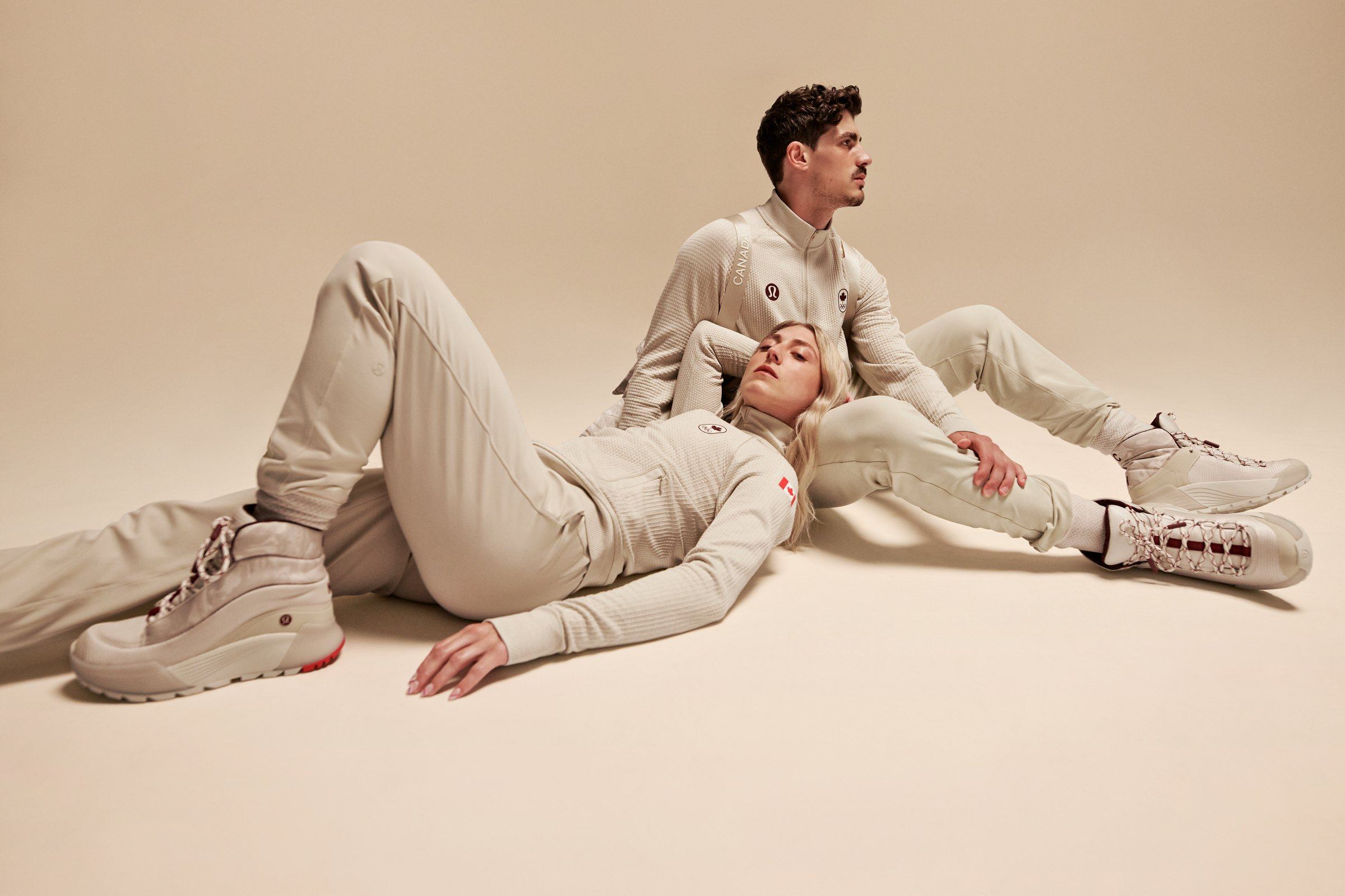 Two athletes in cream Team Canada uniforms reclining on a cream backdrop, wearing the cream closing ceremony boots.