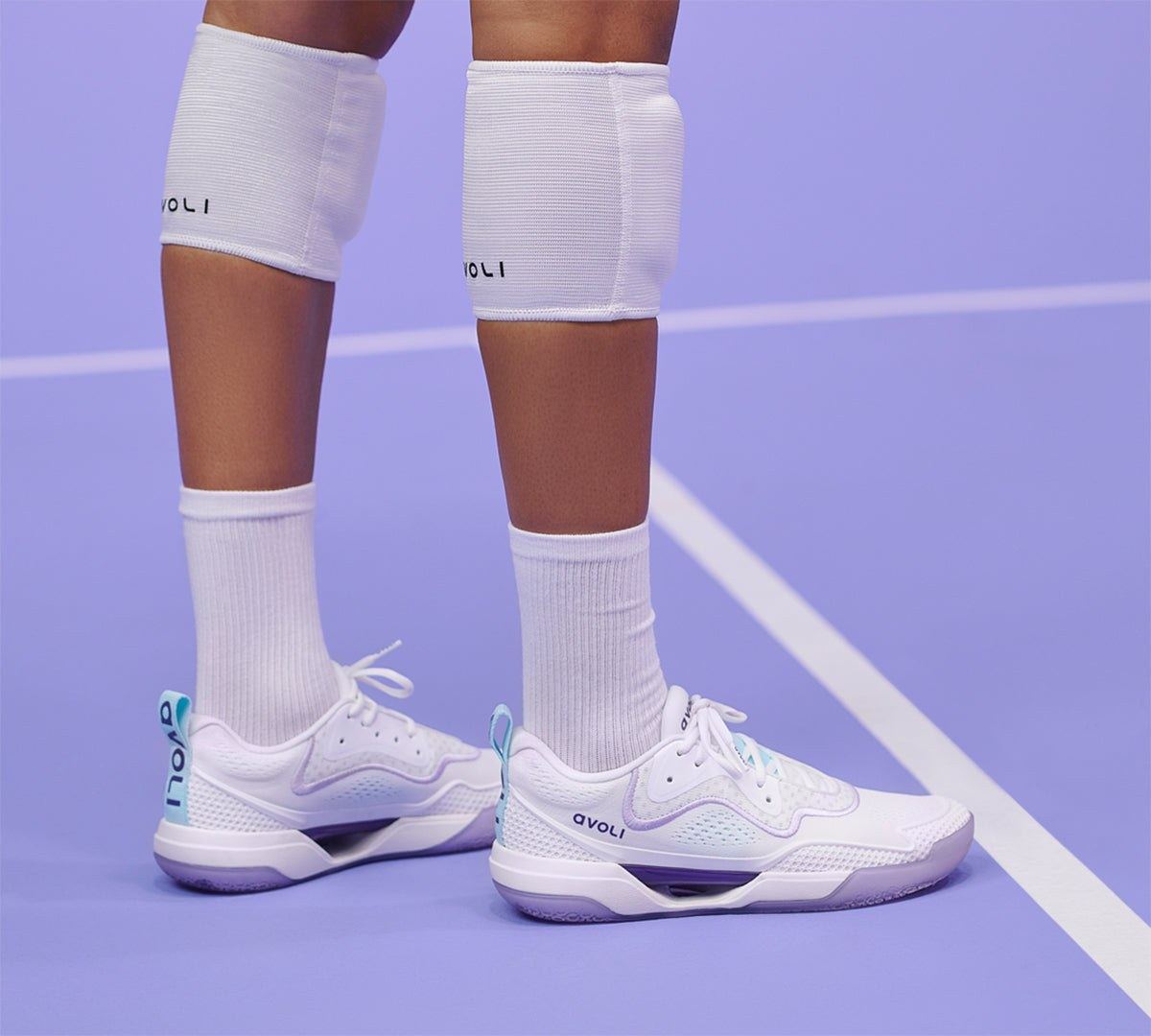A player in white knee pads standing on a lilac court in white Avoli Lows.