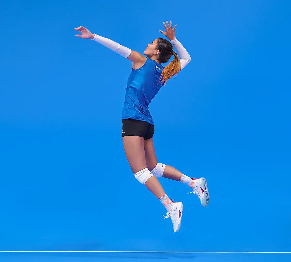 A player in mid-air swinging for a spike against a blue backdrop.