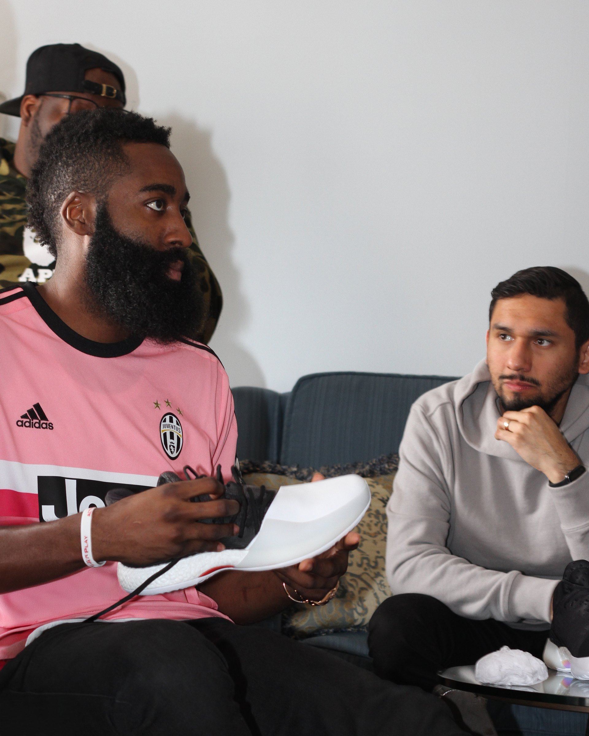 James Harden holding a Harden Vol. 1 sample with a white upper during a sample review, with a member of the design team seated beside him.